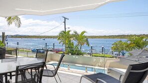 A balcony with a glass railing overlooking a swimming pool and a body of water. - Noosa Moorings 1 Noosaville (Noosaville)