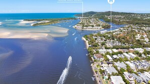 An aerial view of Noosa Main Beach with clear waters, a marina, and residential buildings along the coastline.