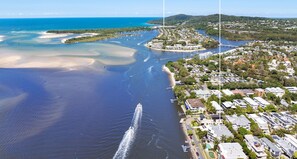 Vista aérea de la playa principal de Noosa, con aguas cristalinas, un puerto deportivo y edificios residenciales a lo largo de la costa.