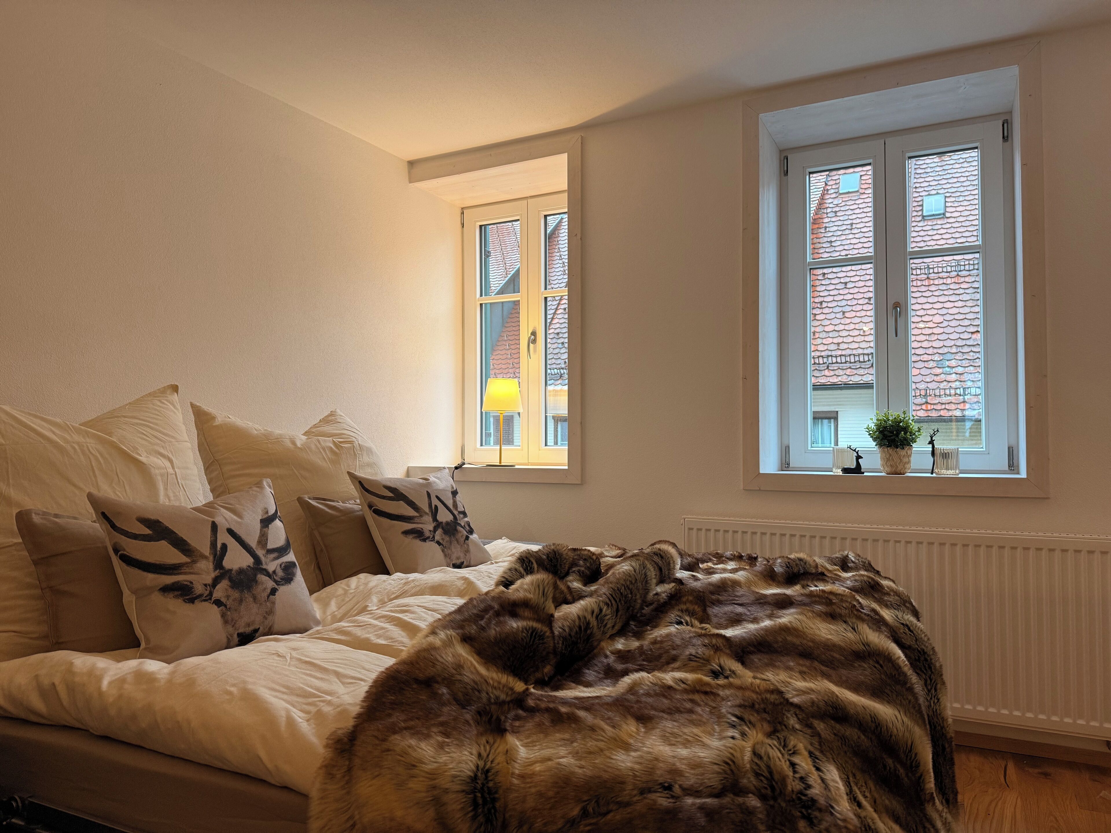 A bedroom with a bed, a window with a view of buildings, and a radiator.