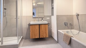 Ein modernes Badezimmer mit einer Glasduschkabine, einem Holzbadezimmerwaschtisch, einem großen Spiegel und einer Badewanne.