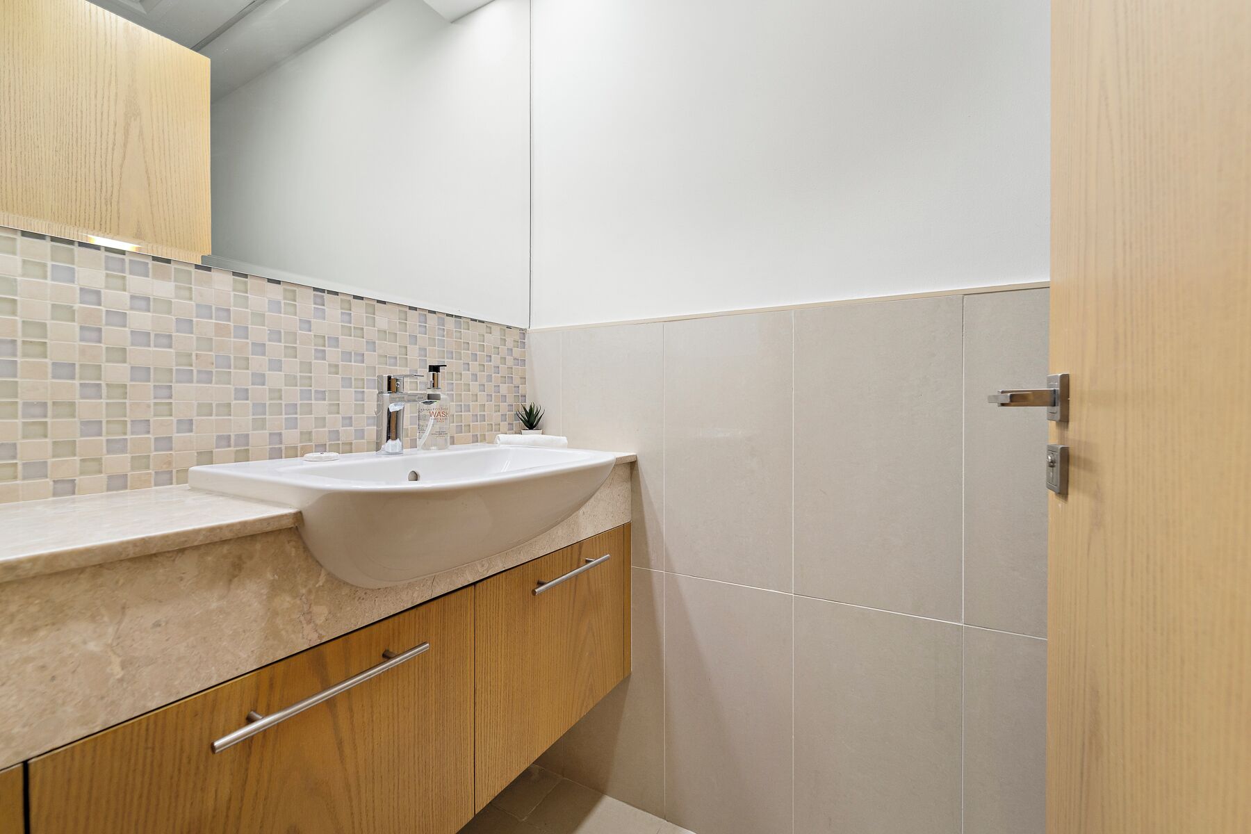 Un baño moderno con lavamanos blanco, armarios de madera y un reverso de azulejos.