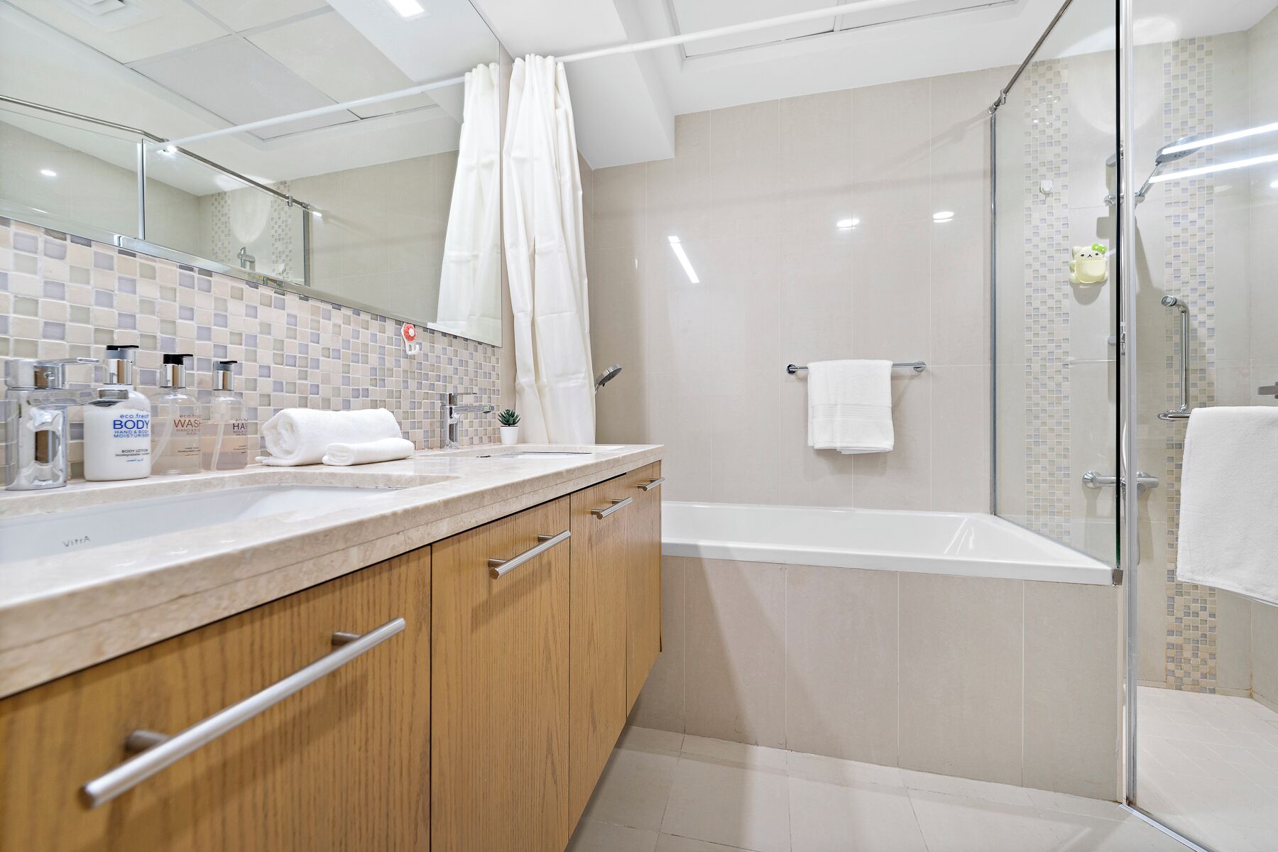 Une salle de bain moderne dotée d’une douche à parois de verre, d’une baignoire et d’un meuble-lavabo avec un miroir et des articles de toilette.