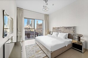 A modern hotel bedroom with a large bed, a nightstand, a mirror, and a view of the cityscape through large windows. - 2BR 203 Bellevue Tower 1 (Dubai)