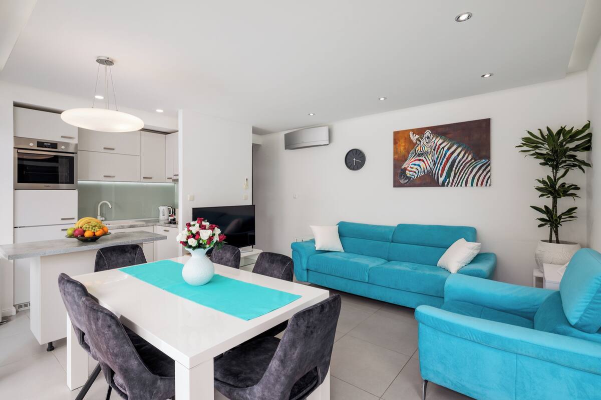 A modern living room with a blue sofa, a dining table with chairs, a TV, and a painting of a zebra on the wall.