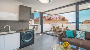 A modern apartment with a kitchen, a washing machine, a dining area, and a sofa with a view of the city. - Villa Muller Apartments (Split)