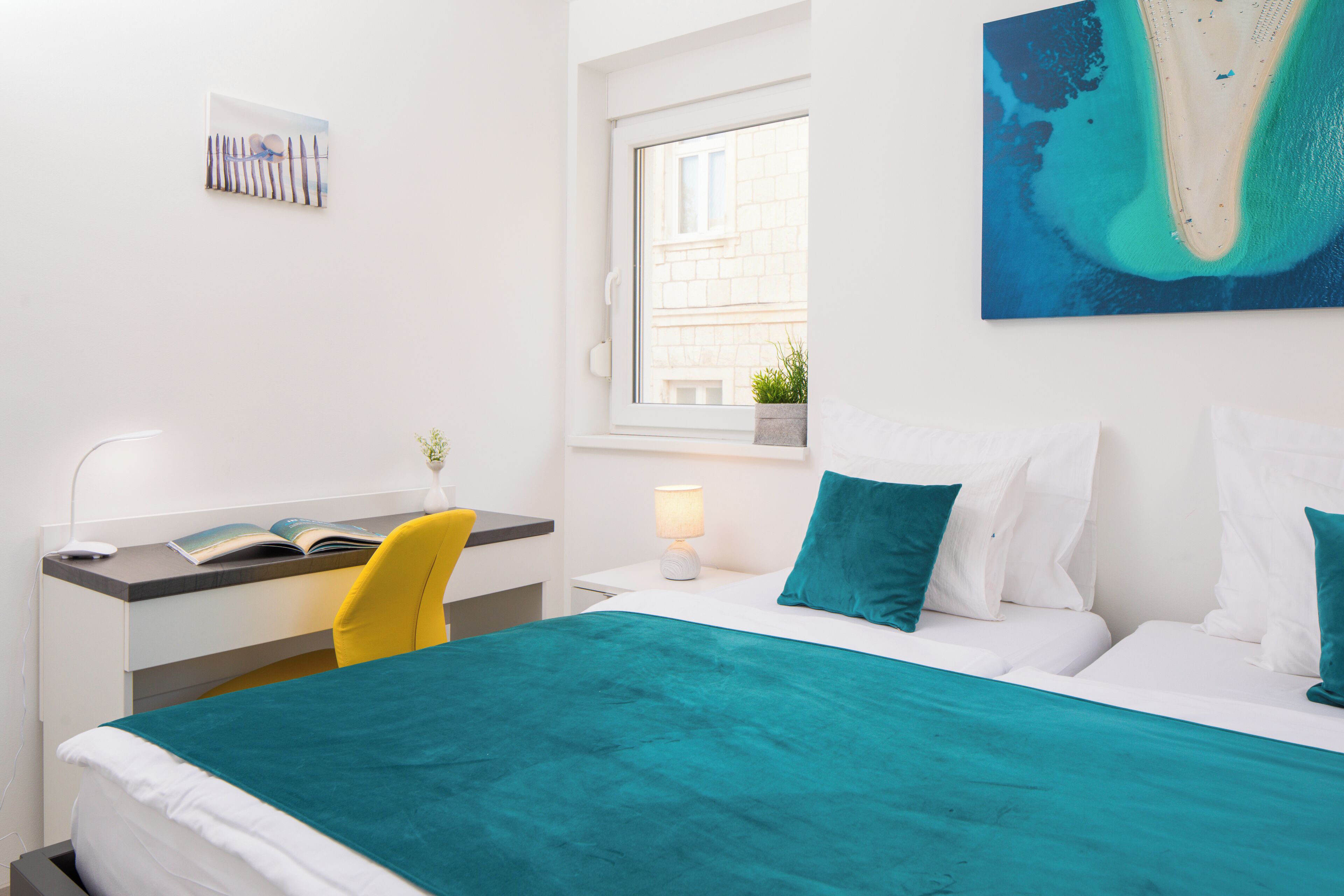 A hotel room with a bed, a desk, a chair, a window, and a painting on the wall.