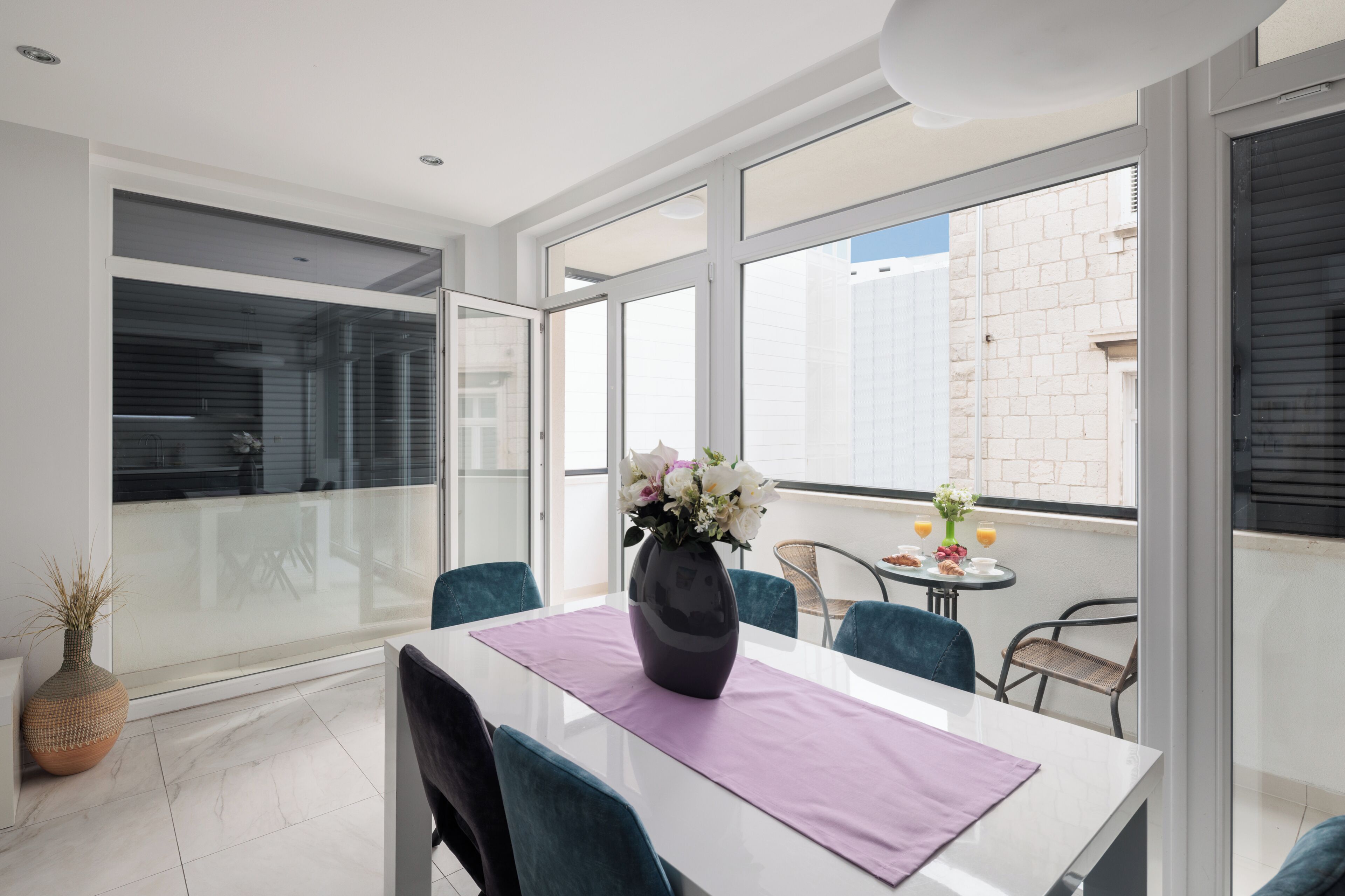 A modern dining area with a white table, purple placemat, and a vase of flowers.