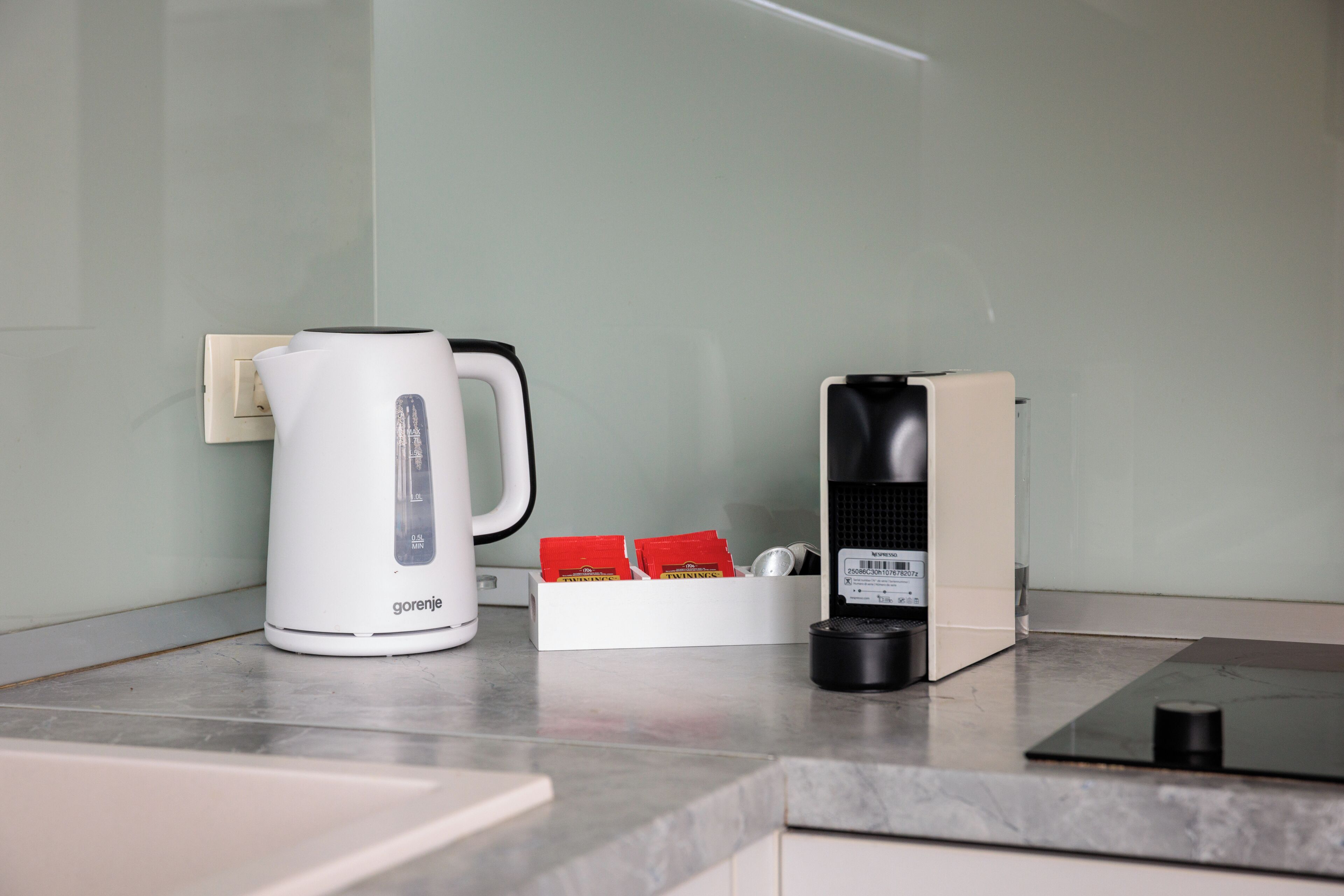 A kitchen with a white coffee maker, a box of red coffee pods, and a black coffee pod holder on a marble countertop.