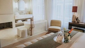 Ett modernt hotellrum med badrum, en sittgrupp och ett matbord som är dukat med en flaska champagne och glas.