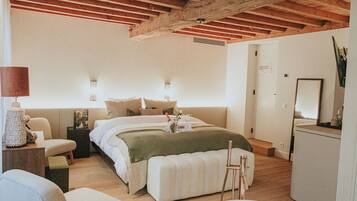 Een slaapkamer met een houten plafond, een bed met een groene deken, nachtlampjes, een bureau met een lamp en een stoel.