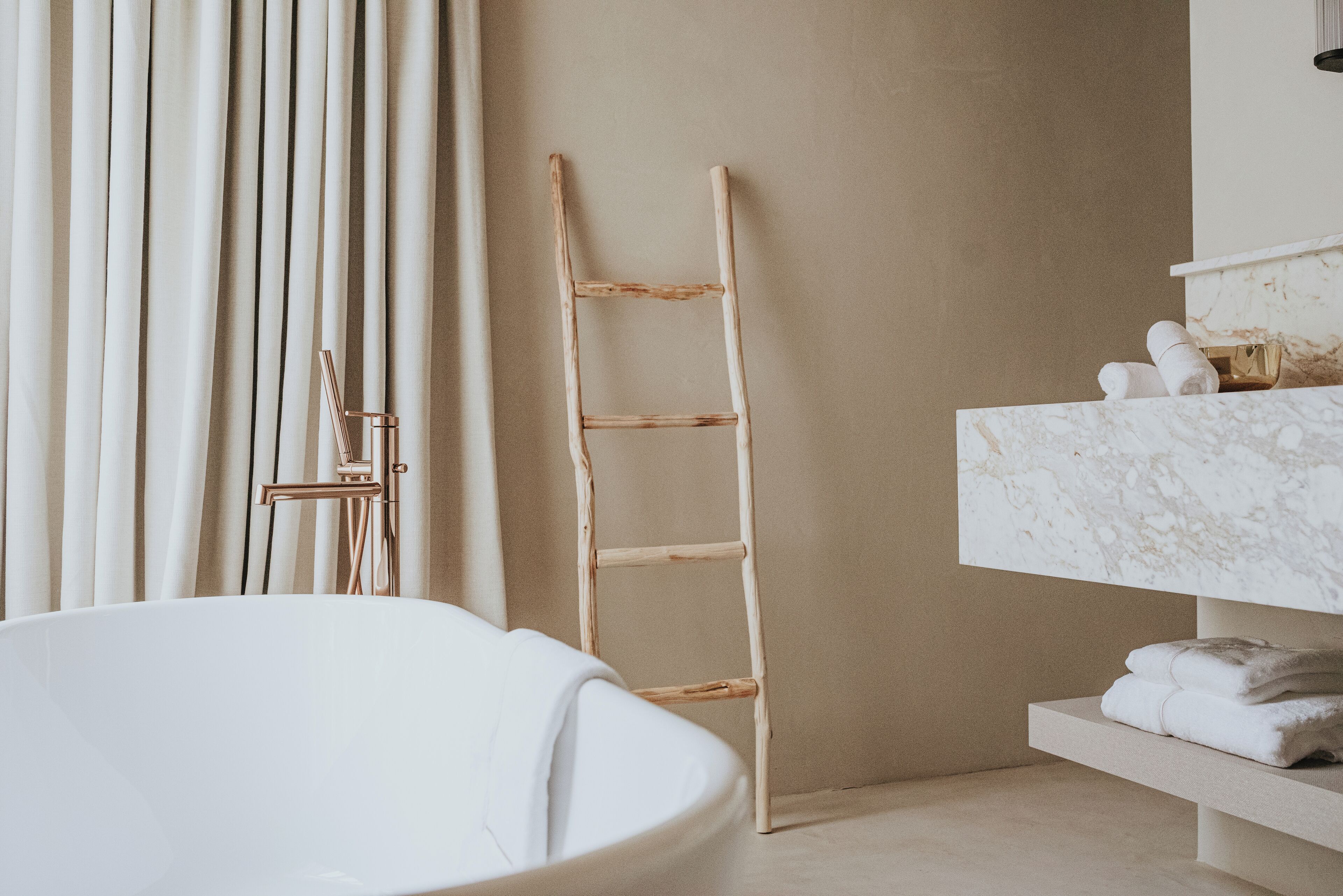 Un baño con una bañera independiente, una escalera de madera, un tocador de mármol y un perchero para toallas.