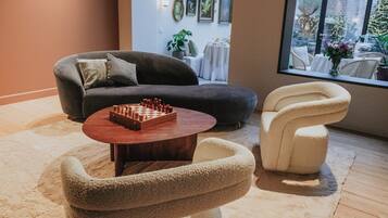 A cozy living room with a chessboard on a wooden table, a grey sofa, and a white armchair.