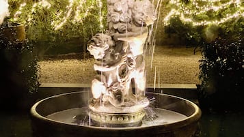 A fountain with a decorative sculpture, surrounded by greenery and illuminated lights.