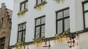 En vit byggnad med svarta fönsterramar, en svart dörr och små krukväxter vid entrén.