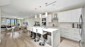 A modern kitchen with white cabinetry, a central island with bar stools, and a view of the outdoors through large windows.