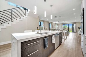 A modern kitchen with a central island, built-in appliances, and a staircase leading to an upper level.