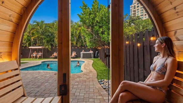 A wooden structure with a pool, benches, and a view of a backyard with trees and a building in the background. - 6 BR Villa Steps to Ocean, Pool, Sauna & Jacuzzi (Fort Lauderdale)