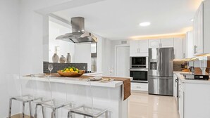 A modern kitchen with a central island, stainless steel appliances, and clear bar stools. - 6 BR Villa Steps to Ocean, Pool, Sauna & Jacuzzi (Fort Lauderdale)