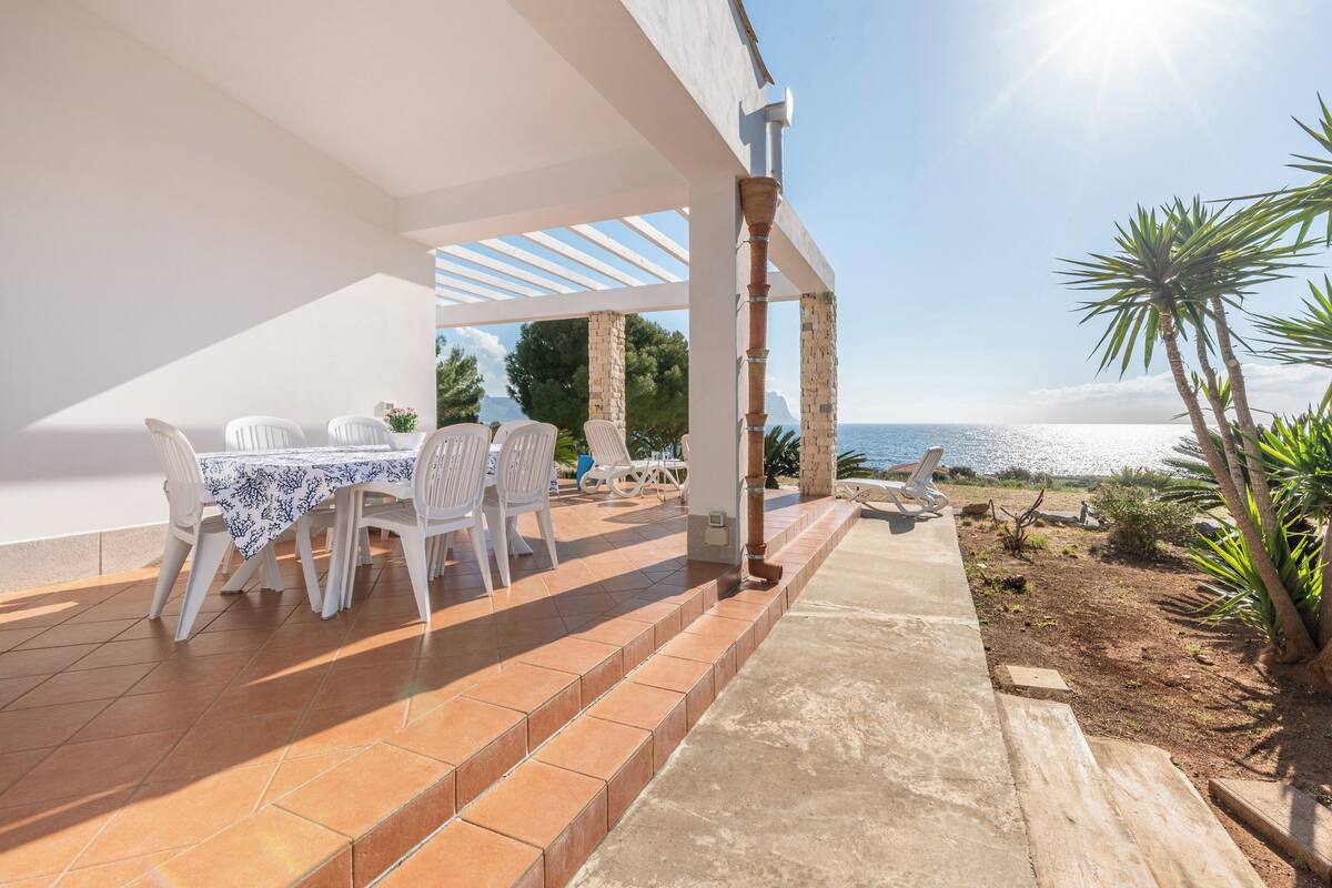 An outdoor patio with a table and chairs, a pergola, and a view of the sea.