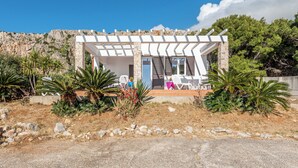 Una casa moderna con fachada blanca, pilares de piedra y un porche cubierto con mobiliario exterior.