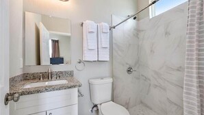 Un baño con pared de ducha de mármol, lavabo con encimera de granito y retrete.