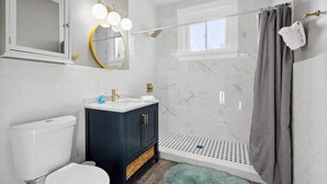 Ein modernes Badezimmer mit Toilette in Weiß, einem dunkelblauen Waschtisch und einer Duschkabine.