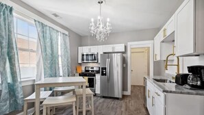 A modern kitchen with white cabinetry, stainless steel appliances, a chandelier, and a dining area with a table and chairs.