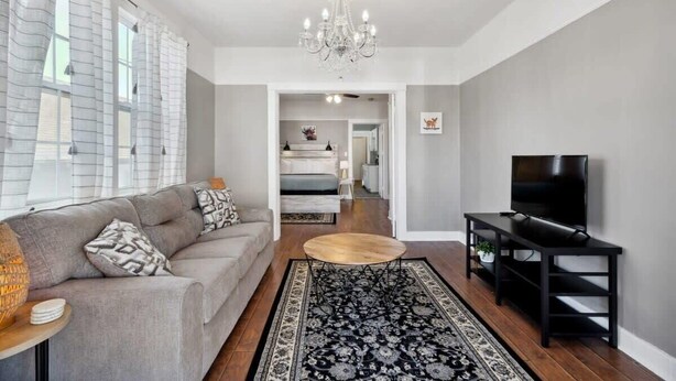 A modern living room with a sofa, coffee table, TV stand, and a chandelier.