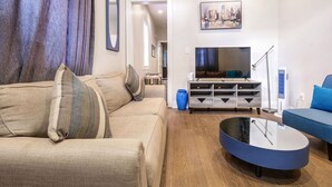 Ein modernes Wohnzimmer mit einem beigen Sofa, einem blauen Sessel, einem Flachbildfernseher, einer Holzunterhaltungsecke und einer blauen Vase.