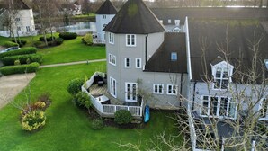 A multi-story house with a prominent tower, surrounded by well-maintained lawns and a small pond. - 'Pepperpot' Lodge on Isis & Windrush Lakes with Great On-site Facilities (South Cerney)