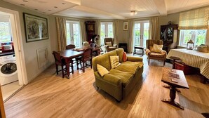 A spacious living room with a wooden floor, a green sofa, a dining table with chairs, and a large window with curtains. - 'Pepperpot' Lodge on Isis & Windrush Lakes with Great On-site Facilities (South Cerney)