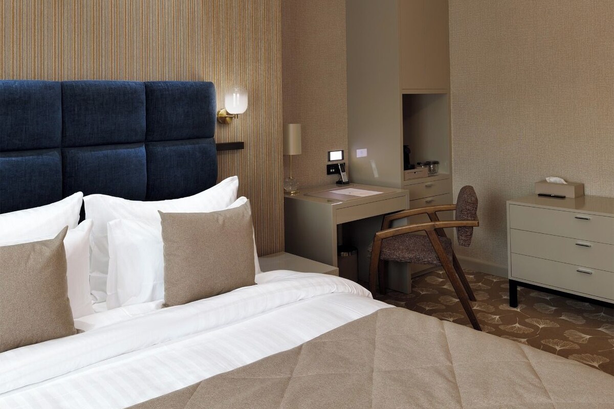 A modern hotel room with a large bed, a desk, and a chair.