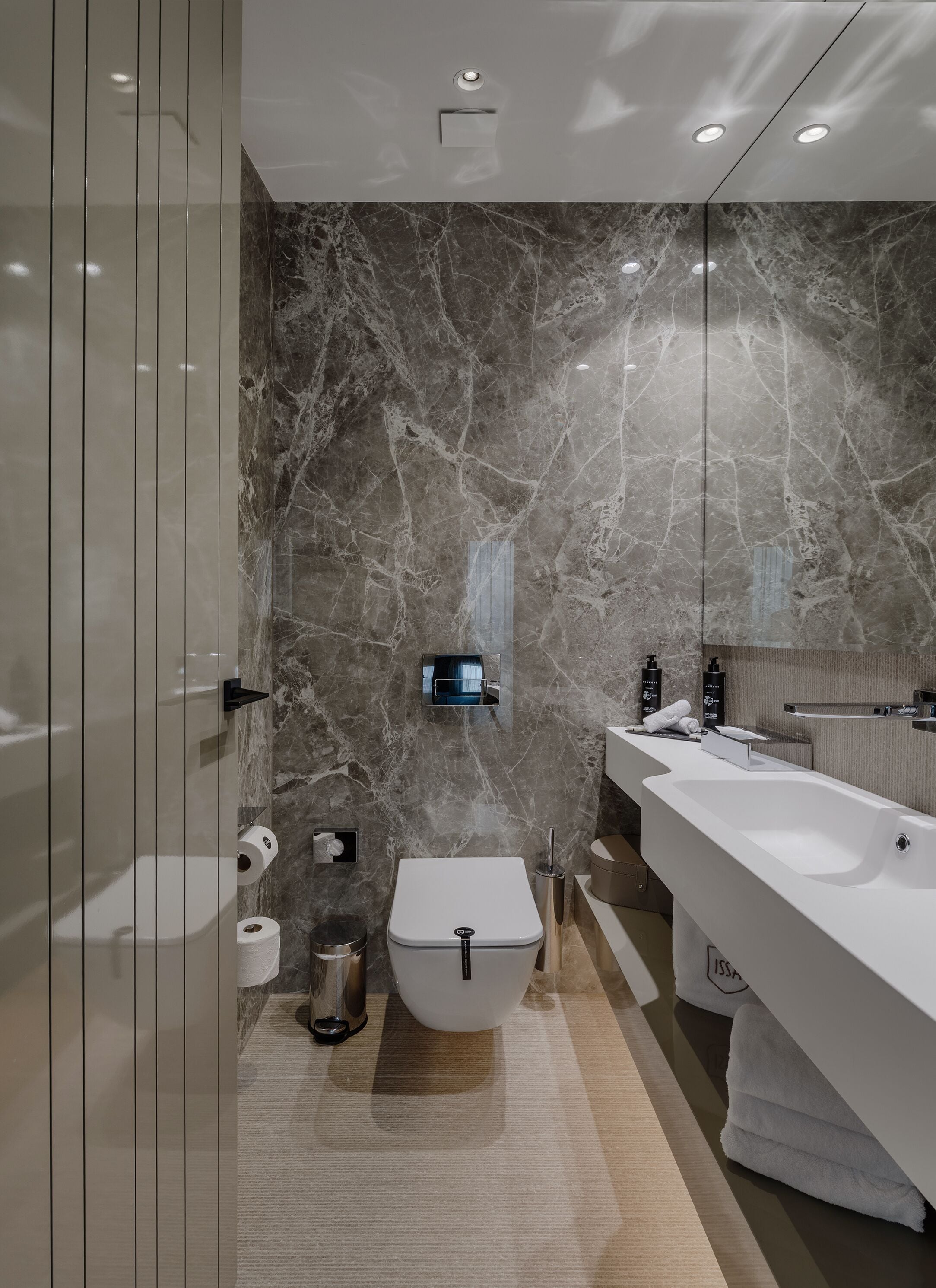 A modern bathroom with a marble wall, a toilet, a sink, and a mirror.