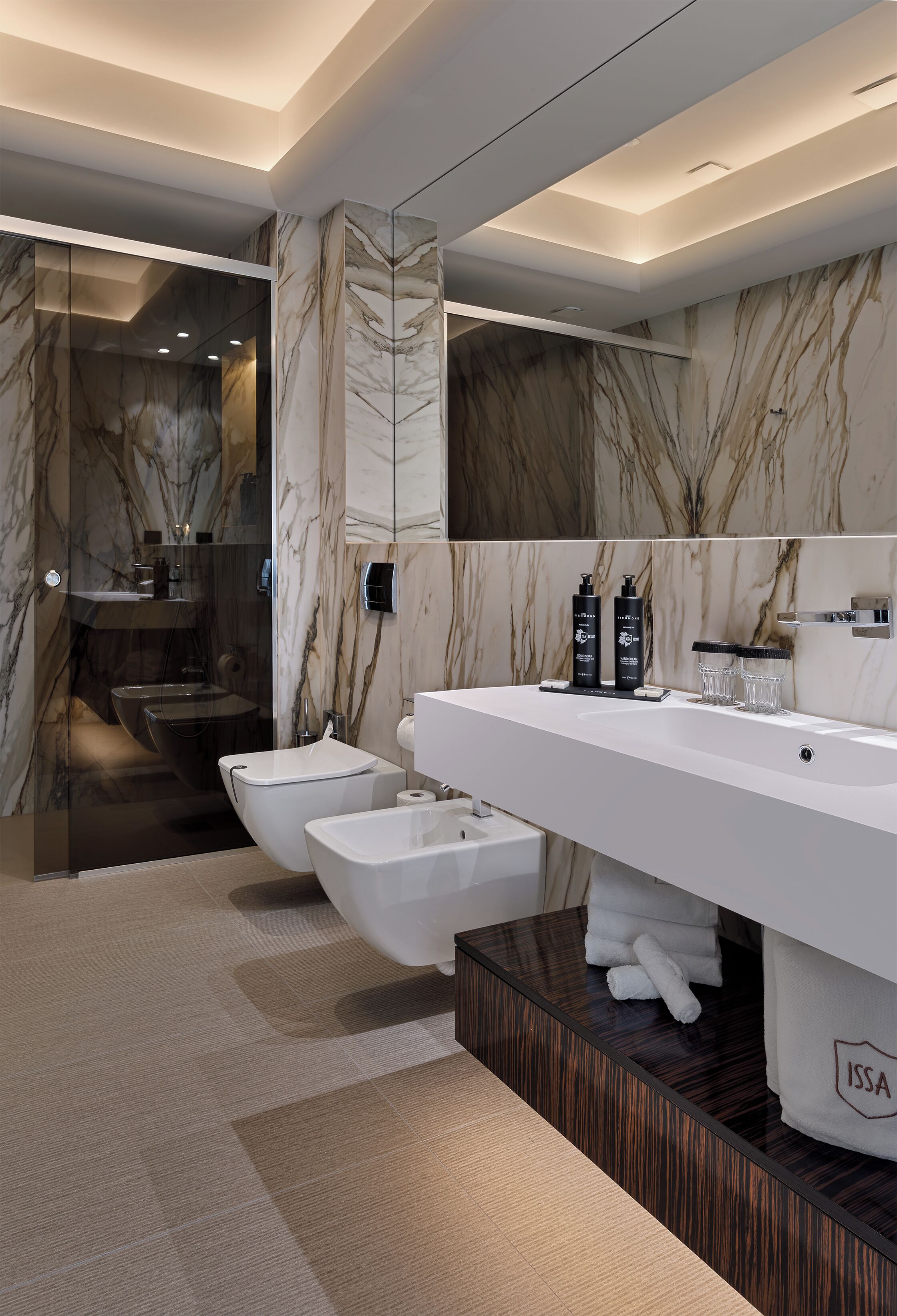 Un baño moderno con un espejo grande, paredes de mármol y un bidé.