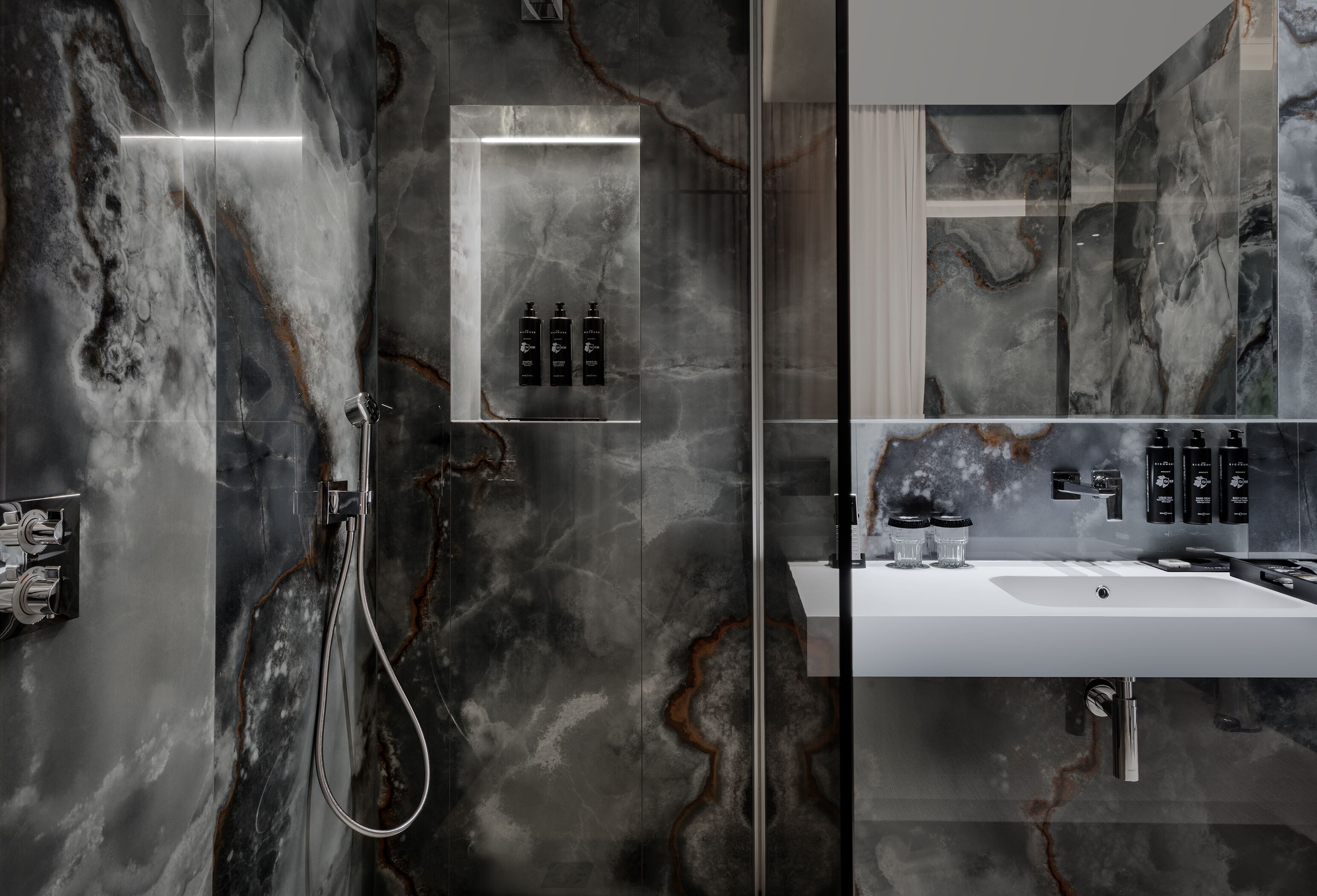 A modern bathroom with a marble wall, a glass-enclosed shower, and a white sink with a mirror above it.