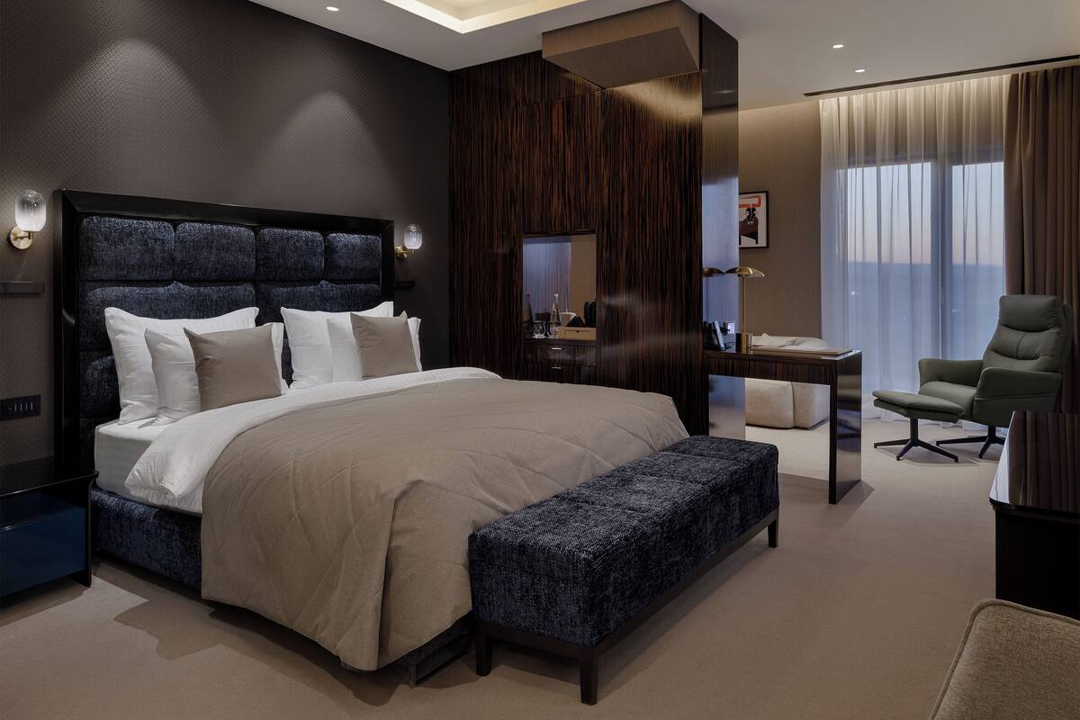 Ein modernes Hotelzimmer mit einem großen Bett, einer Bank, einem Schreibtisch und einem Stuhl.