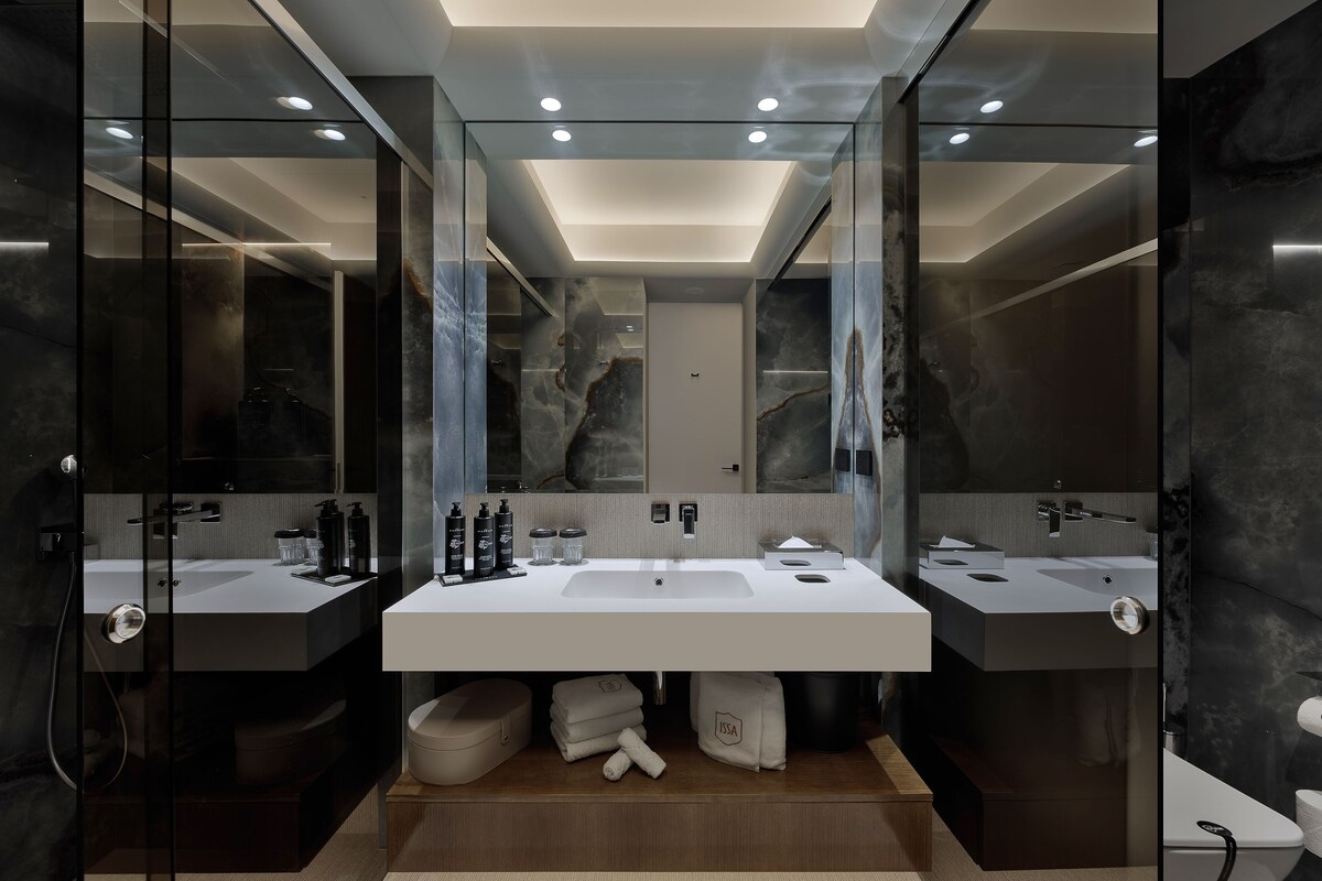 A modern bathroom with a large central sink, two side sinks, and a glass-enclosed shower area.