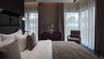 A hotel room with a large bed, a chair, a nightstand, and a vase with flowers.