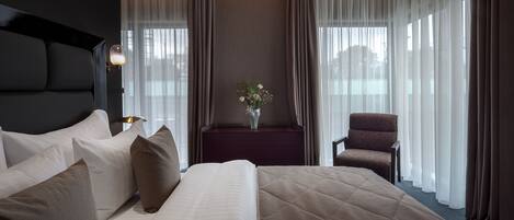 Una habitación de hotel con una cama grande, una silla, una mesita de noche y un florero con flores.