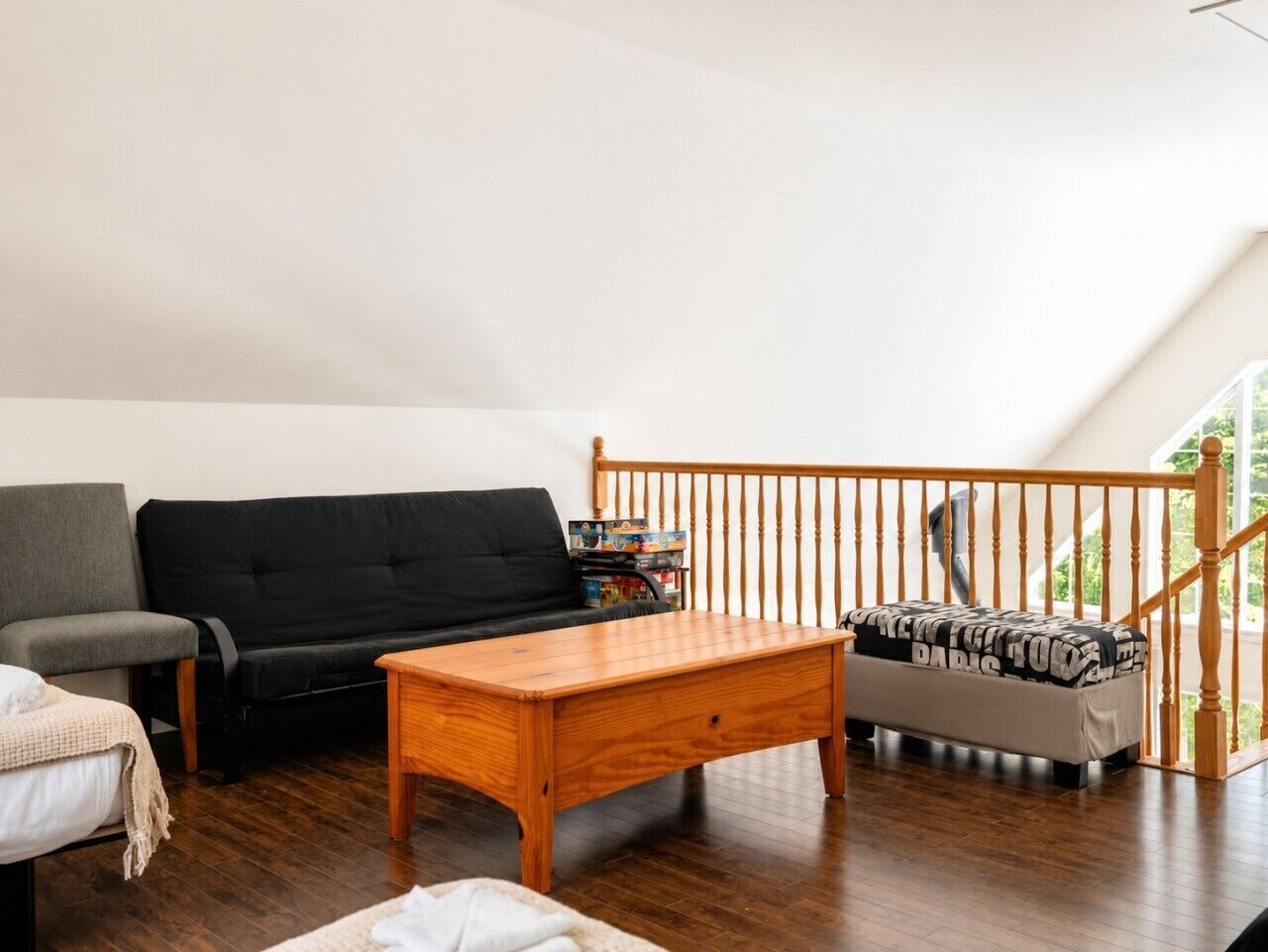Una sala de estar con una mesa de centro de madera, un sofá negro, un sillón gris y una escalera con barandilla de madera.