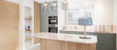 A modern kitchen with a central island, pendant lights, and a built-in oven.
