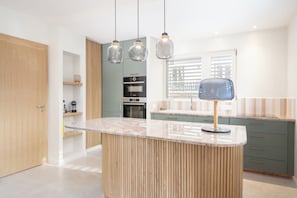 A modern kitchen with a central island, pendant lights, and a built-in oven.