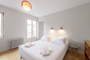 A hotel room with a large bed, a radiator, a small table, and a window with a view. - Le Blanc Meix - 8 guests - Sauna, near the lake, Gérardmer (Gérardmer)