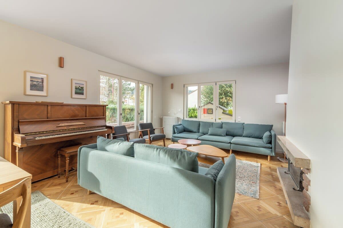 Ein Wohnzimmer mit Klavier, einer Sofagarnitur, einem Couchtisch und einem Kamin.
