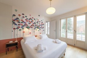 A hotel room with a large bed, a bedside table, a wall-mounted lamp, and a view through the window.