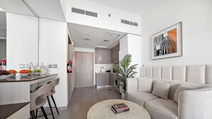 Un salon moderne avec un canapé beige, une table basse ronde et une cuisine en arrière-plan.