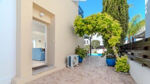 A narrow outdoor corridor with a blue chair, a white air conditioning unit, and potted plants. - Villa Kos #7 - Charming Paralimni Getaway (Protaras)