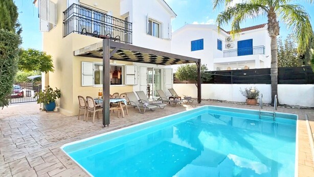 A swimming pool with lounge chairs and a pergola, surrounded by a two-story building with balconies. - Villa Kos #7 - Charming Paralimni Getaway (Protaras)