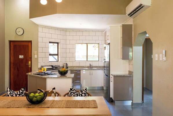 A modern kitchen with a central island, a dining area with a table and chairs, and a view of the outside through a window. - First Group Sanbonani Resort (Mbombela)
